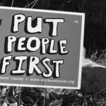 yard sign with Put People First printed on it; a hen in the grass behind the sign