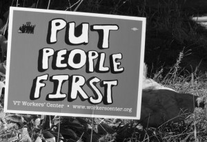 yard sign with Put People First printed on it; a hen in the grass behind the sign