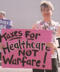 woman holding pink sign with black text: "Taxes For Healthcare NOT Warfare"
