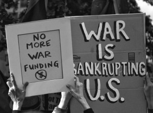 hands holding up signs saying No More War Funding and War is Bankrupting U.S.