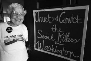 Frances Crowe next to a handwritten cursive sign saying, "Arrest and Convict the Serial Killers in Washington"