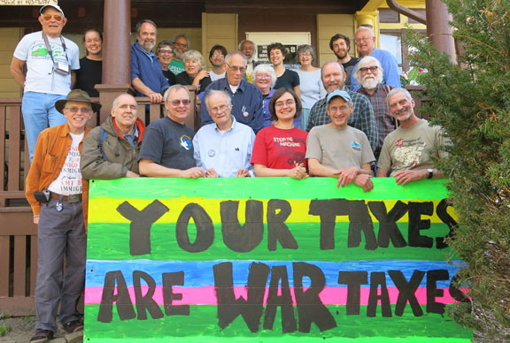 Conference attendees posing behind a large sign that reads “Your Taxes are War Taxes”