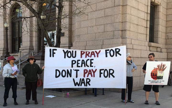 Protesters hold sign reading “If you pray for peace, don’t pay for war”