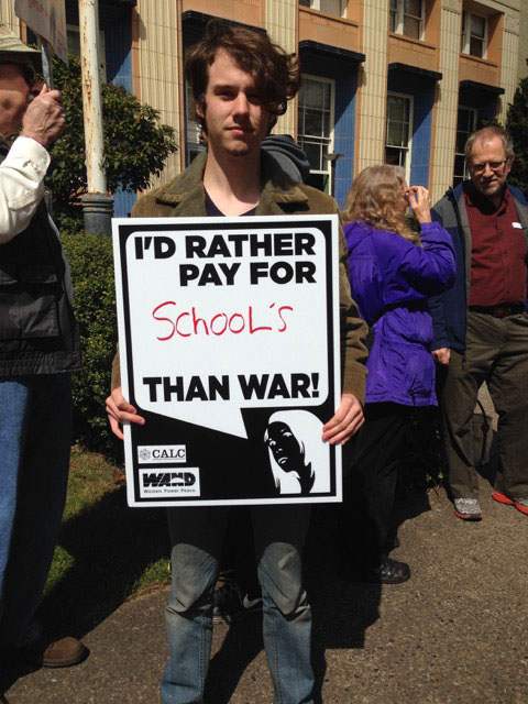 Man holds sign reading “I’d rather pay for school’s than war!”