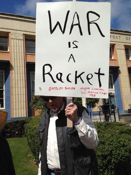 Man holds picket sign reading “War is a Racket” (Smedley Butler)