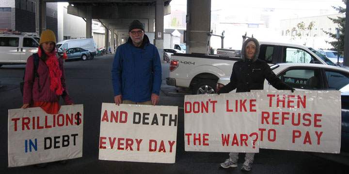 Four people holding signs that have this message, printed sequentially: “Trillions in debt” / “and death every day” / “don’t like the war?” / “then refuse to pay”