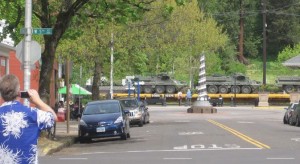 photo of train passing through intersection while carrying tracked vehicles