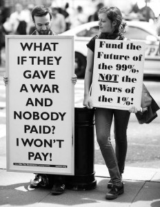 two protesters with signs: “What if they gave a war and nobody paid? I won't pay!” and “Fund the future of the 99%, not the wars of the 1%!”