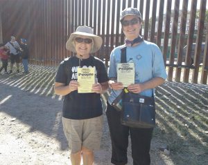 Anne and Erica standing at the border with NWTRCC's "Divest from war, invest in people" flyers (Spanish text on the back!)