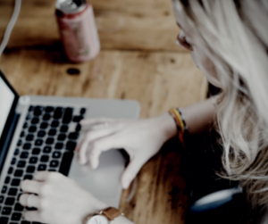 image from the left side of a white woman with long blonde hair typing at a laptop