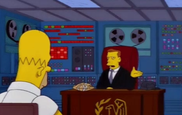 Homer Simpson sits in front of an IRS agent at a desk, with an old supercomputer on the wall behind the agent