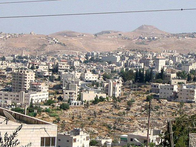 a photo of desert hills in the distance with Beit Sahour, composed of many white short and medium sized buildings in the middle and foreground