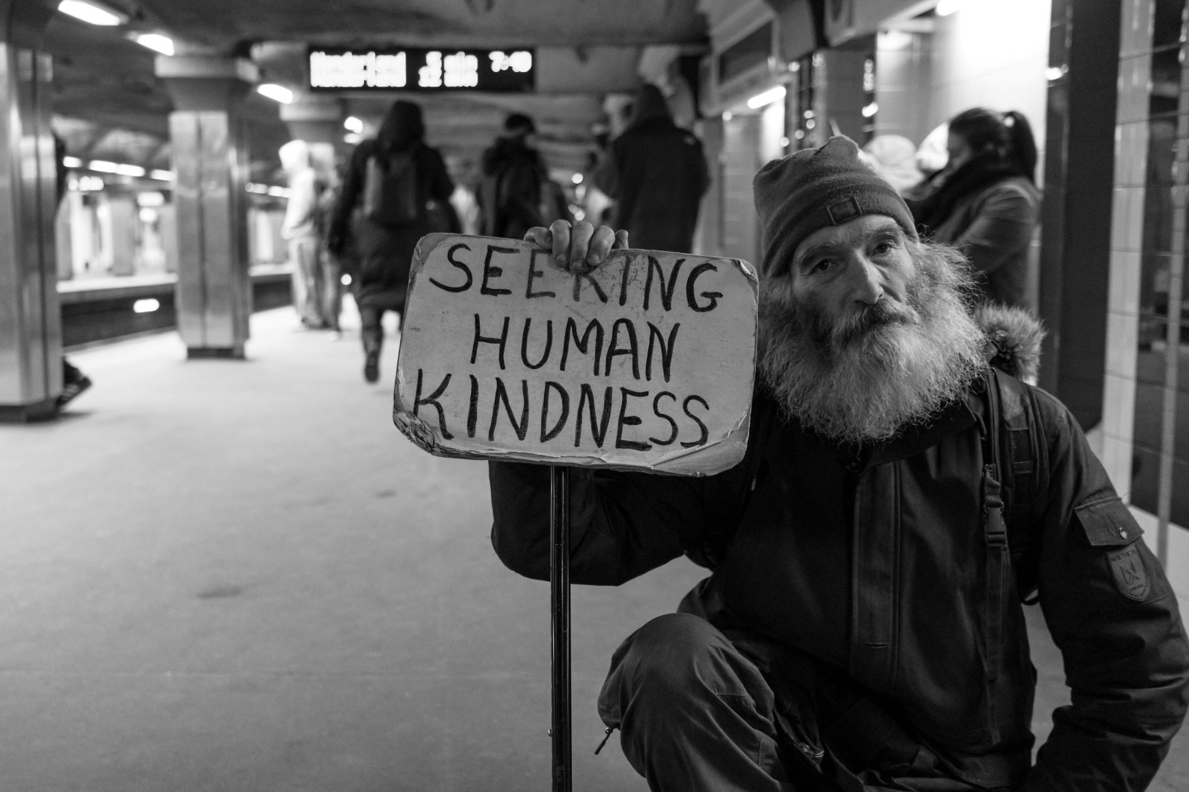 Man holding a sign reading"Seeking Human Kindness "
