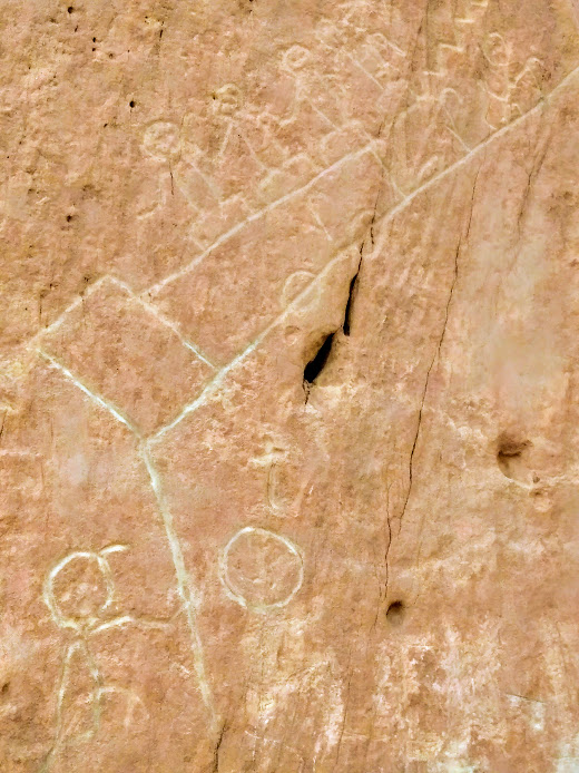 pertoglyh on stone with images of "stick" people facing two paths- one with a locomotive running away (representing modern technology) and another path that includes farming corn and living close to the earth
