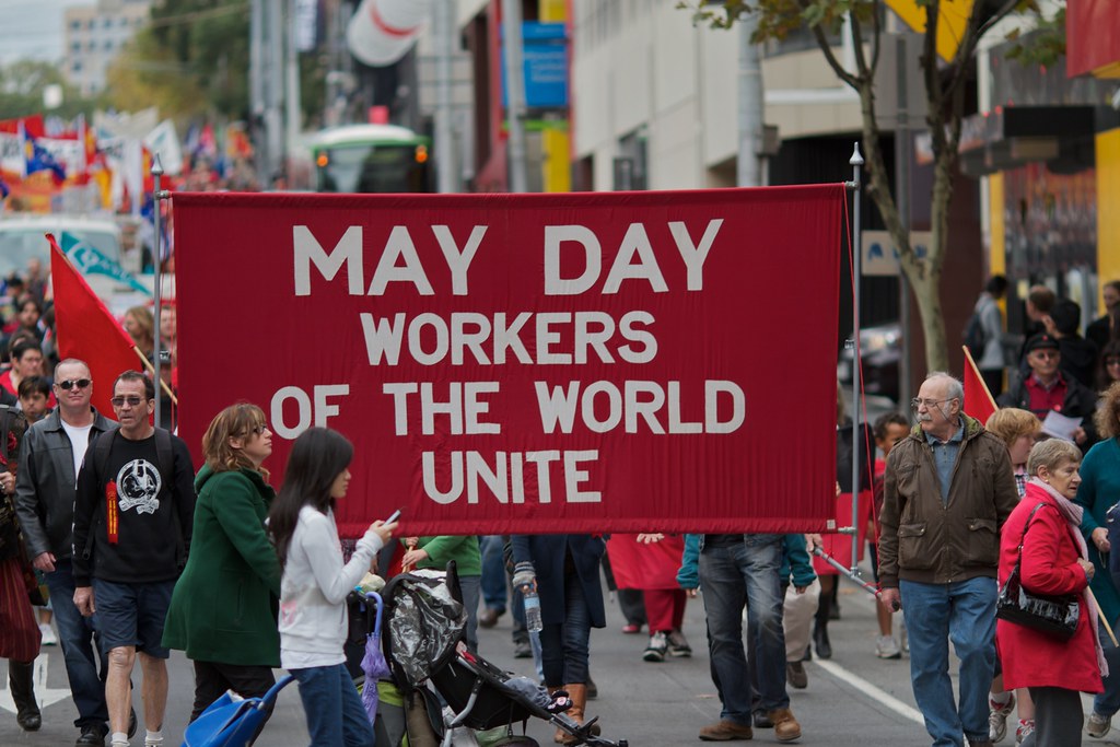 People in the street around a banner that states MAY DAY Worker of the world unite