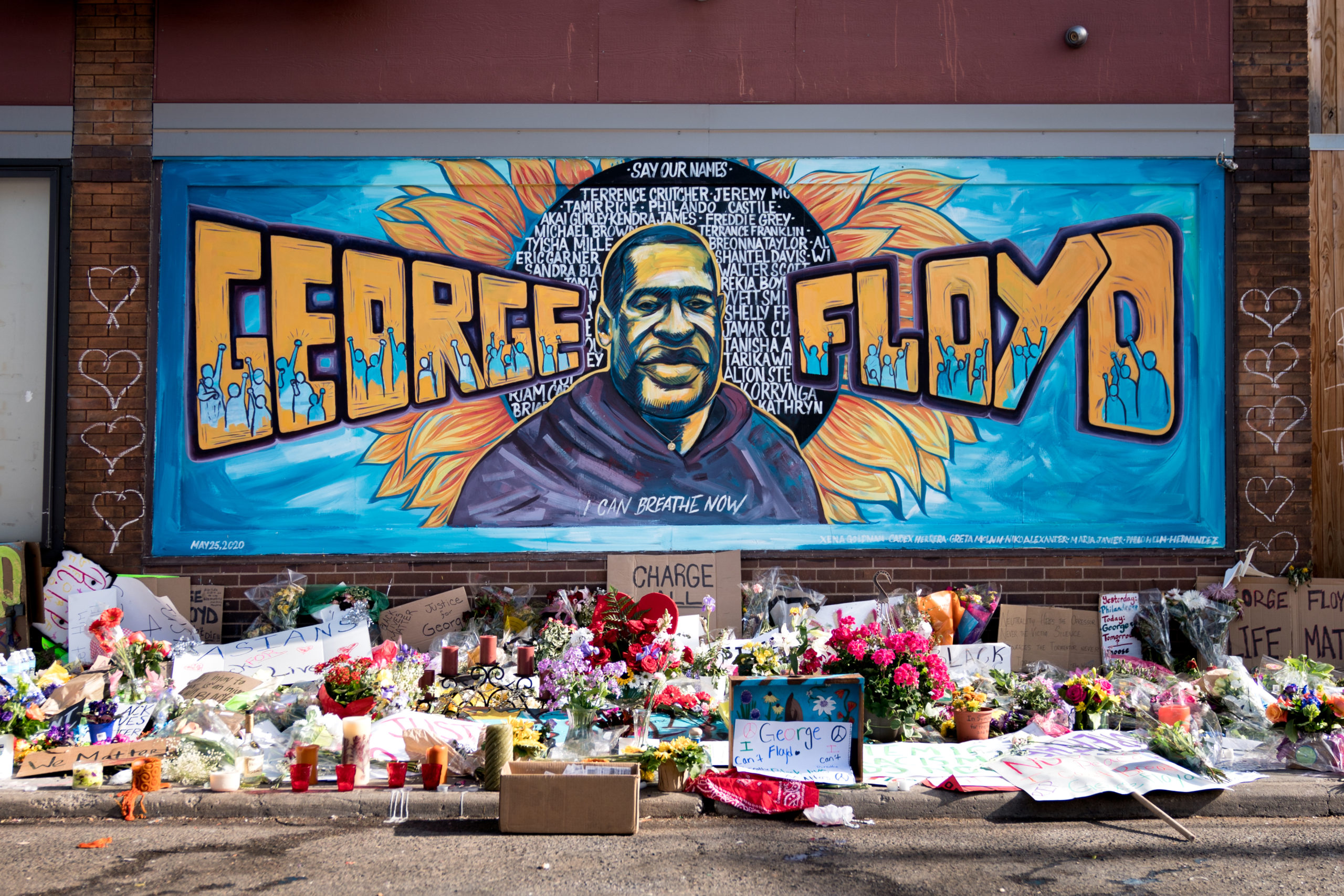 mural on the side of building with flowers and objects placed on ground as a memorial