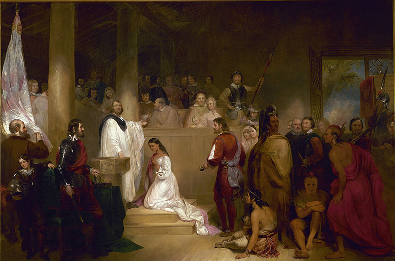 Gathering of 30 people who are surrounding a woman in white kneeling in front of a man in white who appears to be speaking to the crowd