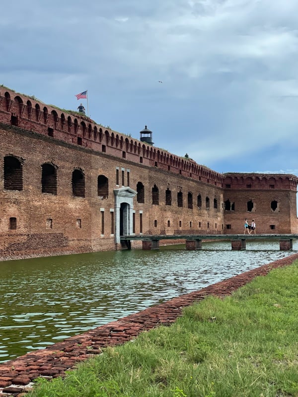 large brick structure in background with water surrounding it and grass in the lower side