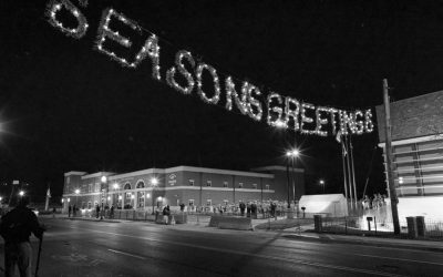 seasons greetings in lights above a street with Ferguson police officers in background