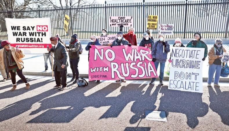 people sanding against a fence in the background holding signs and banners one in pink that reads no war with Russia