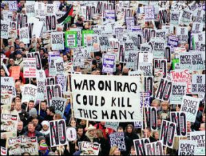 large gathering of people not clearly visible wih many signs ; one in lower portion of picture with sign reading War on Iraq could kill this many